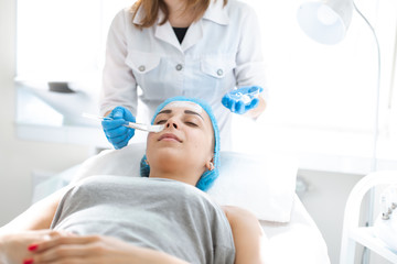 Naklejka premium Woman professional doctor beautician applies a mask on a patient's face for skin care. Cosmetic procedures for skin rejuvenation and nutrition