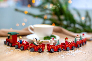 Delicious fresh festive morning cappuccino coffee in a ceramic white cup on the wooden table with decorative christmas train, red ornamentals, fireflies and spruce branches