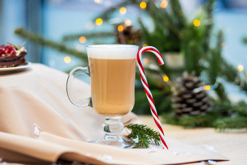 Delicious cappuccino coffee cup and Christmas candy sweet. fireflies and spruce branches background.