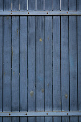 Part of an old wooden fence with boards painted blue gray. The boards are arranged vertically with two cross-nails. Vertical orientation.