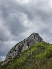 Impressive, rocky, pointy summit Asenovo kale, dramatic cloudy sky and beautiful sunlit, vivid green forest during early spring