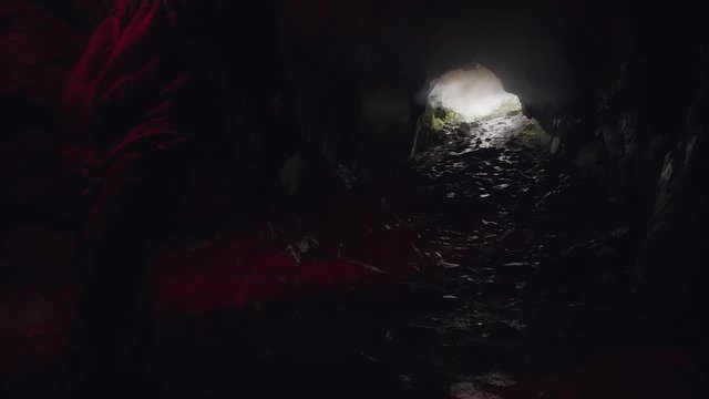 Man lighting his way inside dark cave with a burning signal flare and leaving the entrance behind him. Stock footage. Dangerous tourism inside dark grotto.