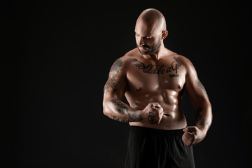 Fototapeta premium Athletic bald, bearded, tattooed man in black shorts is posing against a black background. Close-up portrait.