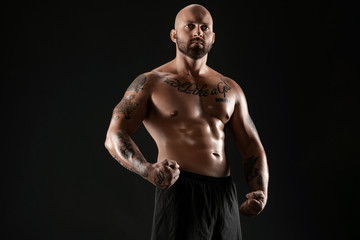 Naklejka premium Athletic bald, bearded, tattooed man in black shorts is posing against a black background. Close-up portrait.