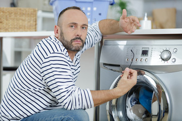 man making gesture of incomprehension towards broken washing machine