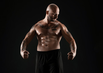 Obraz na płótnie Canvas Athletic bald, bearded, tattooed man in black shorts is posing against a black background. Close-up portrait.