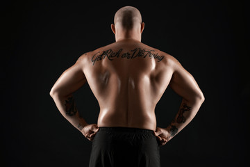 Fototapeta premium Athletic bald, bearded, tattooed man in black shorts is posing against a black background. Close-up portrait.