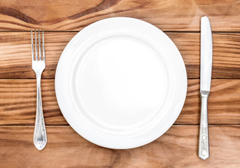 Empty plate with fork and knife on the brown wooden table. Top view.