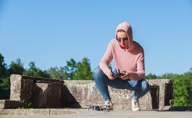 Fototapeta premium A young woman in a pink hoodie and sunglasses controlled with the remote control drone landing in nature.