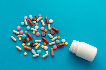 A handful of colored pills spilled out of the can on a blue background. Medical concept