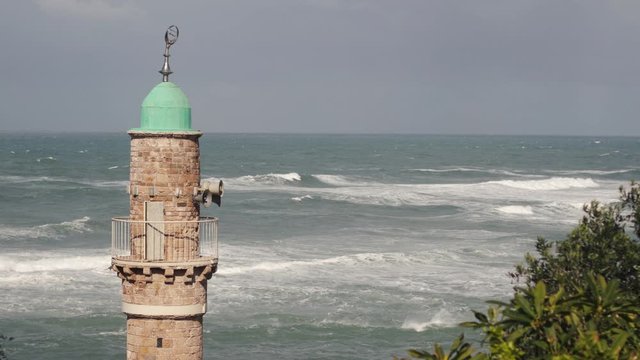 Close up of a Mosque tower, watching over the mediterranean sea, in the old city of Jaffa. Strong waves, of after a storm, in the background.