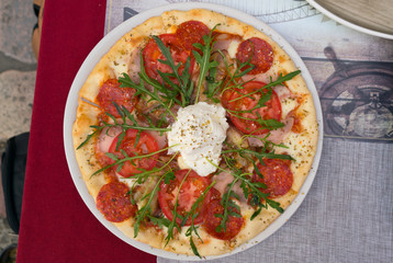 Fototapeta na wymiar pizza with salami, tomatoes and arugula on a plate