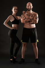 Fototapeta na wymiar Athletic man in shorts and sneakers with brunette woman in leggings and top posing on black background. Fitness couple, gym concept.