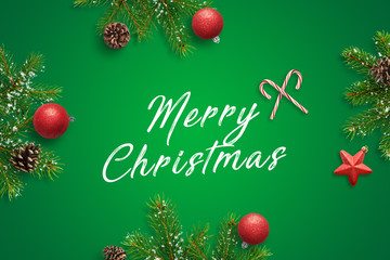 Merry Christmas greeting card. Red balls, star, lollipop, pinecones and fir branches on green surface. Top view, flat lay composition.