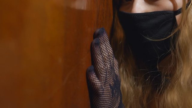 Close-up of a woman in a black mask on his face sitting on the floor near the door.