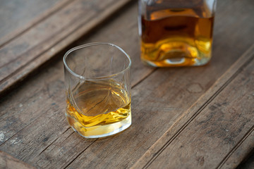Detail of glass and bottle with golden whisky on wooden barrel