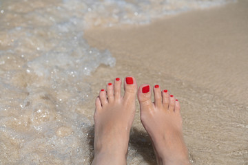 woman legs with pedicure laying on beach with the waves and white sand