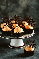 Chocolate cupcakes with pumpkin cream and chocolate spider web. Dessert for Halloween.