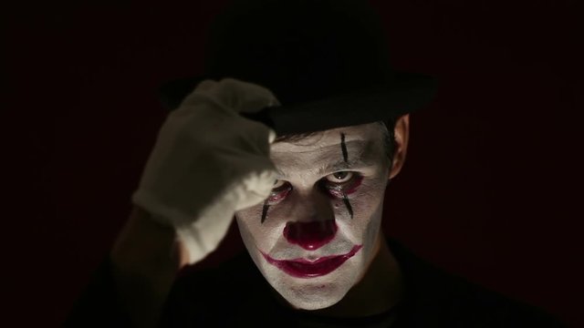 Terrible clown looks at the camera and laughs terribly. Terrible man in a clown makeup takes off his hat by welcoming his victim, looks at the camera and laughs. Halloween.