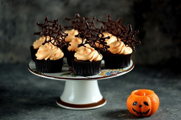 Chocolate cupcakes with pumpkin cream and chocolate spider web. Dessert for Halloween.