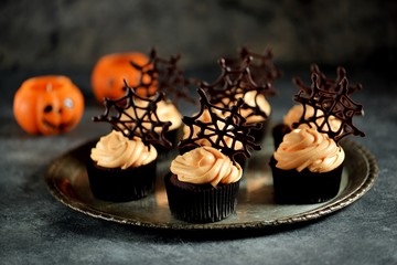 Chocolate cupcakes with pumpkin cream and chocolate spider web. Dessert for Halloween.