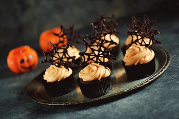 Chocolate cupcakes with pumpkin cream and chocolate spider web. Dessert for Halloween.
