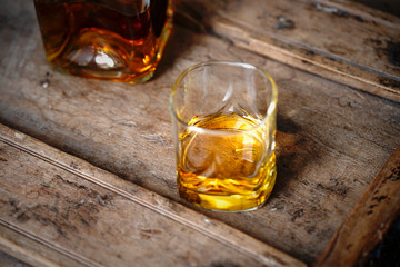 Golden whisky in a glass with light reflections on an old oak table 