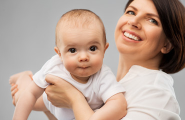 family, child and parenthood concept - happy smiling middle-aged mother holding little baby daughter over grey background