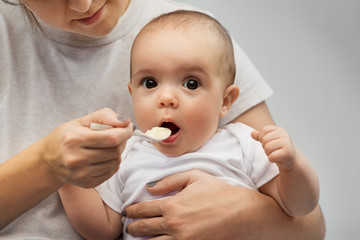 child, eating and food concept - close up of mother with spoon feeding little baby