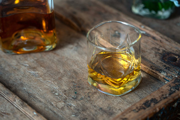 Golden scotch in whisky glass on a barrel in used look in sun light