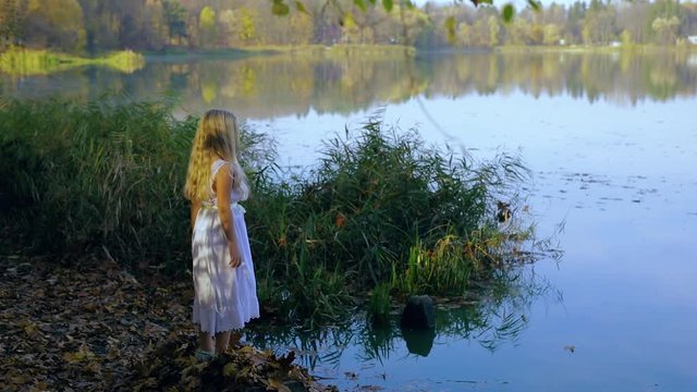 little blond girl in white dress comes to the lake Slow motion side view