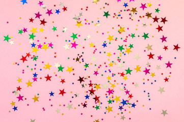 Photo of multi-colored stars glitter sprinkles on pink trendy background. Festive holiday background for your projects. Celebration concept. Christmas pattern. Top view, flat lay