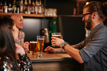 Friends standing next to bar counter in pub and drinking beer. Night out.