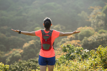 Fototapeta na wymiar Woman ultramarathon runner outstretched arms to sunrise at tropical forest trail