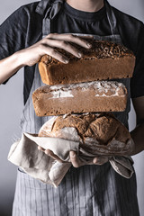 Trzymanie różnych rodzajów chleba w dłoniach na szarym tle w stylu rustykalnym przez osobę w...