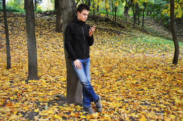 Teenager reads message from smartphone on walk in Park in autumn