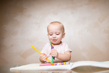 baby girl with a smile looks at the many pencils and crayons held in her hands