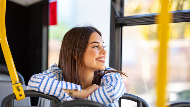 Woman traveler contemplating outdoor view from window of bus. Young lady on commute travel to work sitting in bus or train. Pretty female commuter daydreaming on bus. Young woman taking bus to work