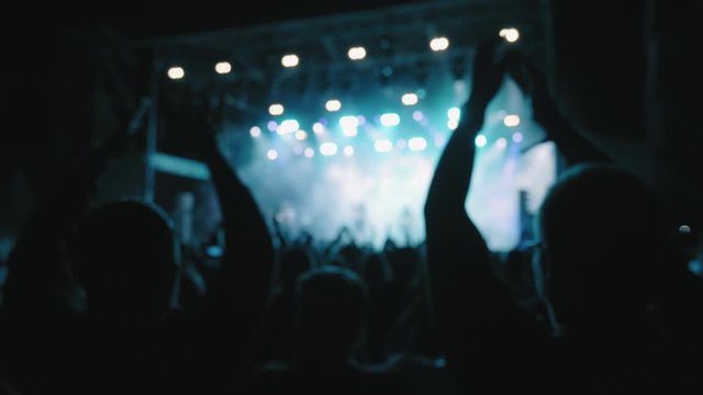 Silhouettes of fans at a music show, concert. Festival of youth rock music. Laser stage show. A crowd of fans raised their hands, applause. Rock symbol made of fingers. Rock concert. Lifestyle