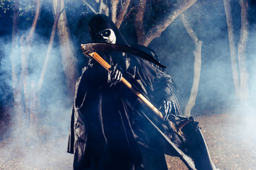 Grim Reaper standing in the fog at night with his scythe.