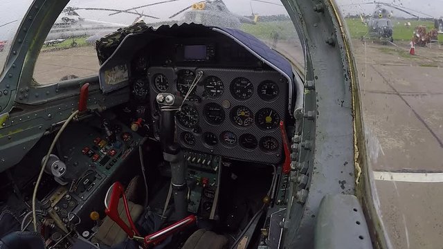 People move a combat fighter plane to a parking spot at the airfield against the background of different helicopters. View of empty cockpit and dashboard close up. First person.