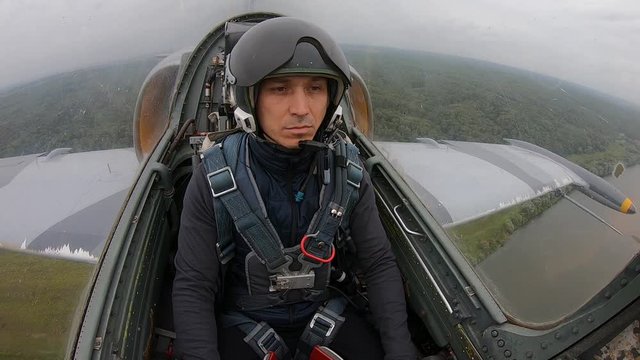 Preparing a new pilot for flights on plane. Gray blue fighter combat aircraft fly over green field and forest in cloudy white sky. Inside view from cockpit close up. Caucasian man in seat.