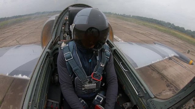 The pilot close helmet and looks around. Gray blue fighter combat aircraft accelerate on the runway at old airfield on a cloudy day. Inside view of cockpit. The plane moves on concrete slabs.