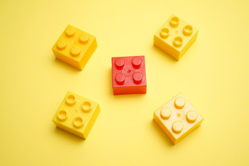 A yellow children's plastic bricks or blocks toy with a unique red color on yellow background