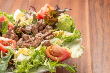 Fresh green salad with arugula,romaine, tomato, eggs, steak mignon and lettuce in a bowl on a wooden  background