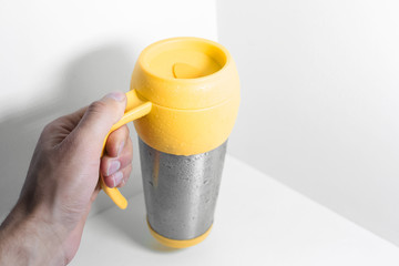 Male hand holding yellow steel thermo mug on white background.