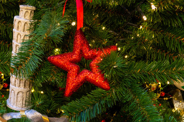 Christmas decorations. Red stars, a toy in the shape of a leaning tower of Pisa, red and silver ribbons, a shining garland decorate the Christmas tree. Close-up