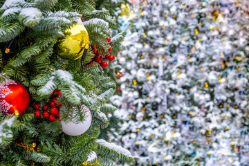 Xmas decorations. Real spruce on the street. Red berries covered with snow. Christmas toys, balls of red and silver colors, weigh on a branch. close-up. Lights unfocused in the background. Macro