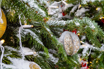 Christmas decorations. Real spruce covered with snow. Christmas tree toy, a ball of white and silver color with a heart on top and a shiny garland hanging on a branch. Close-up. Macro. Xmas
