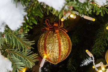 Christmas decorations. Real spruce covered with snow. Christmas tree toy, a ball of red and gold color with a bow on top and a shiny garland hanging on a branch. Close-up. Macro. Xmas